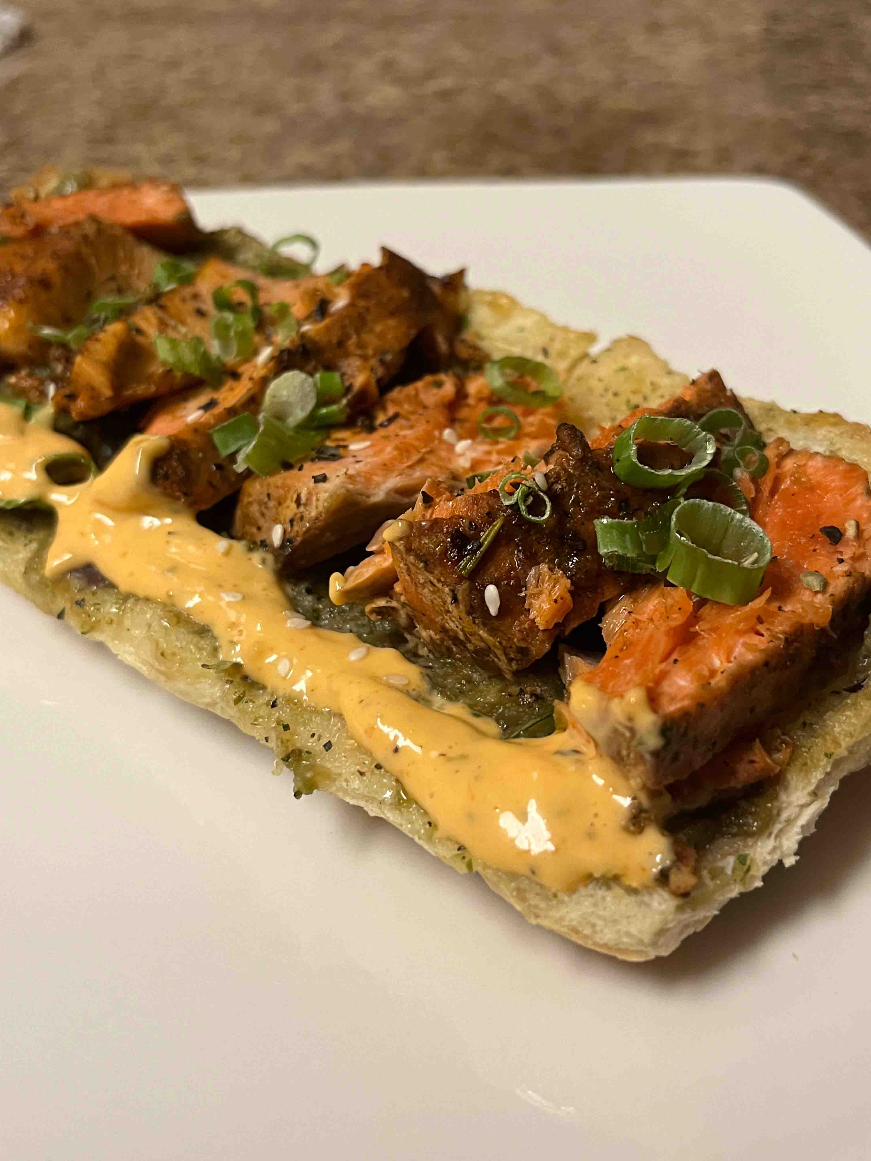 a flatbread topped with salmon, green onions, yellow sauce, and other miscellaneous items