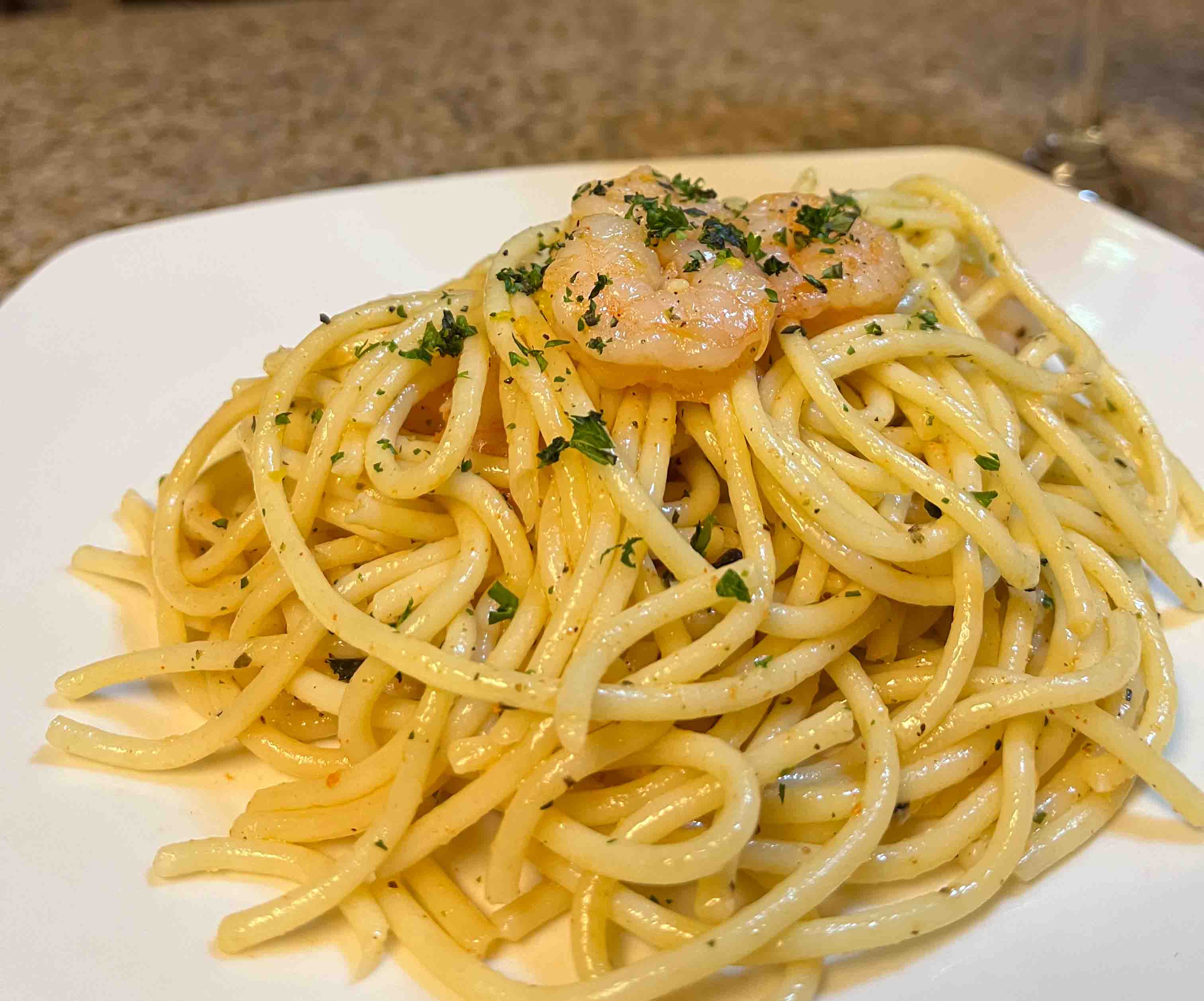 oil based pasta on a white plate, topped with parsley and a few small cooked shrimp