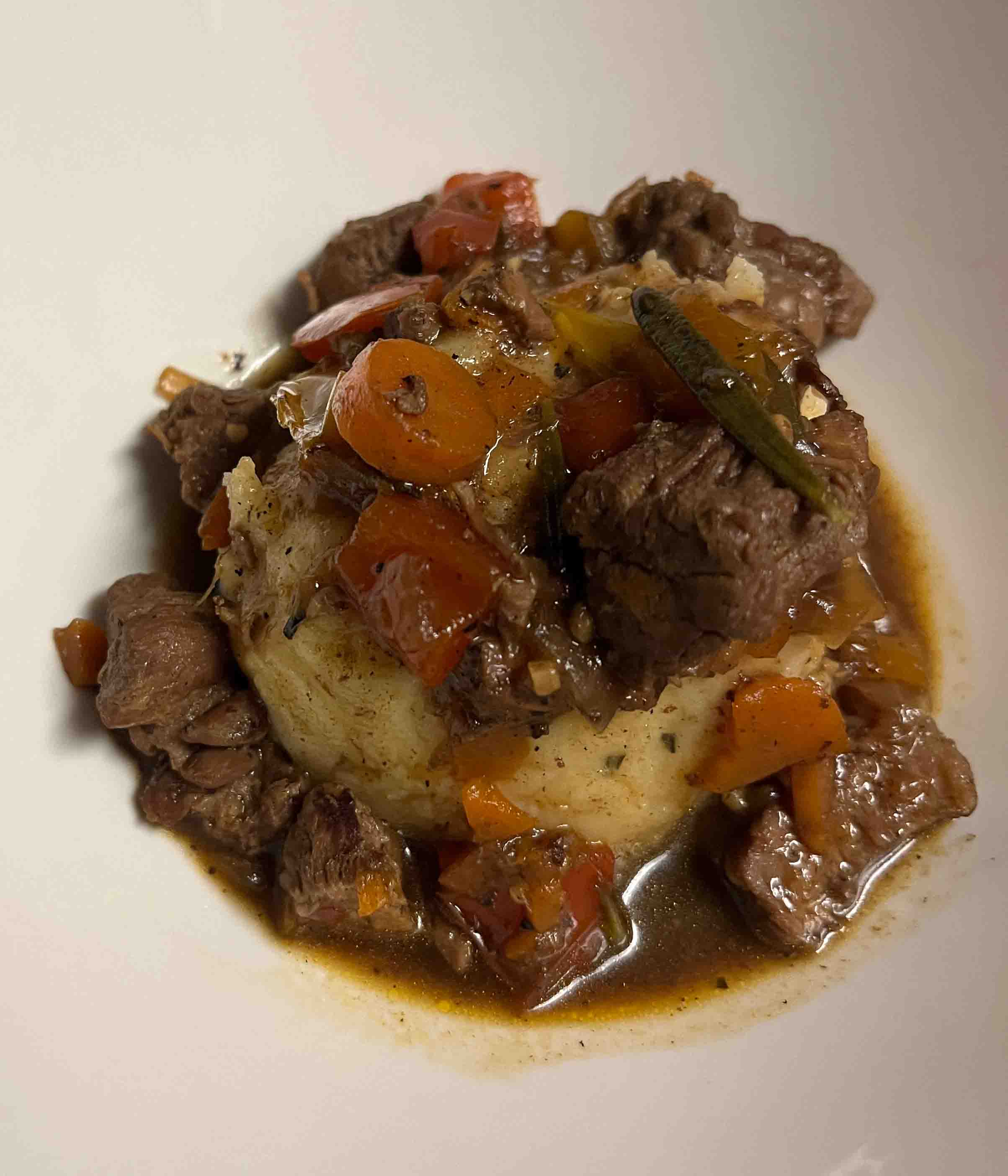 a scoop of mashed potatoes in a bowl, topped with beef chunks, carrots, and stew broth