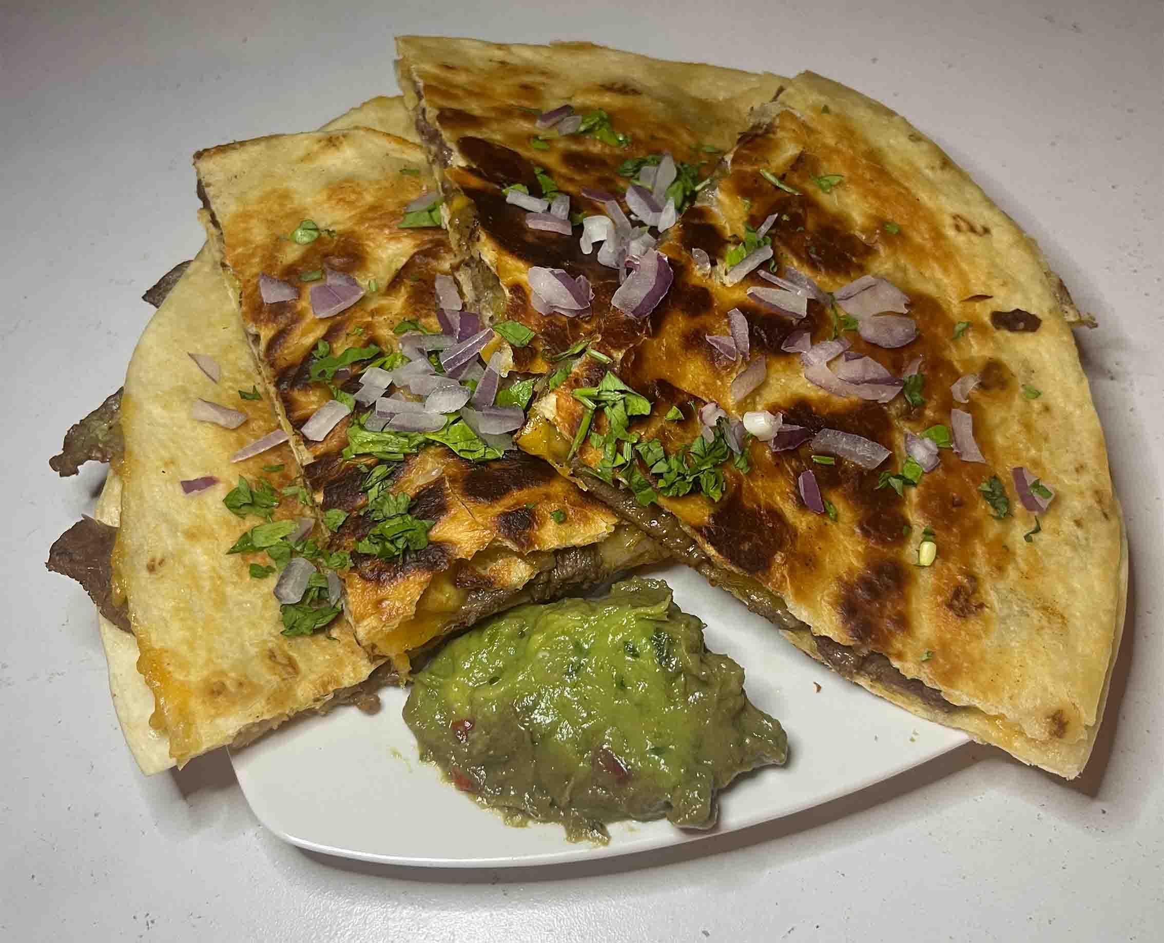 quesadillas on a white plate, topped with red onions, cilantro, and served with a dollop of guacamole